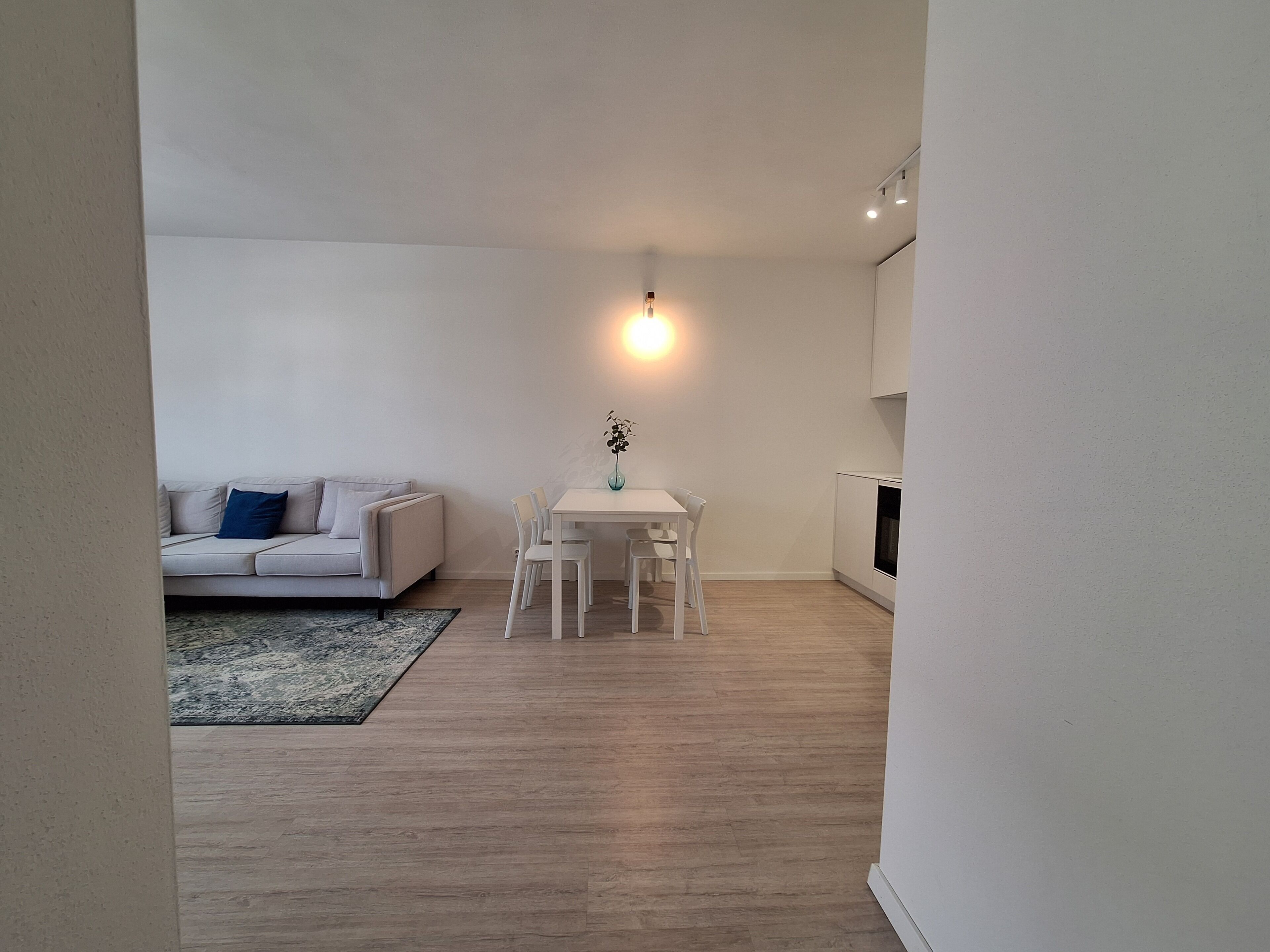 A modern living room with a white sofa, a dining table with chairs, and a small table with a vase.
