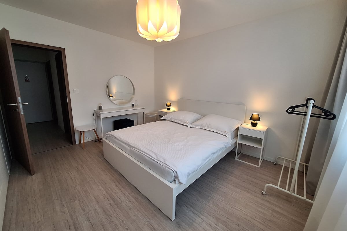 Un dormitorio moderno con una cama grande, mesitas de noche, un espejo y una lámpara colgante.