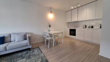 A modern living room with a white sofa, a dining table, and a kitchen area with white cabinets and a built-in oven.