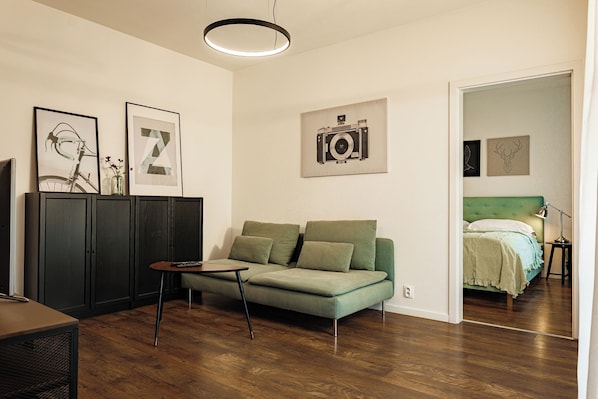 A modern living room with a sofa, a small table, and a television. There are framed pictures on the wall and a bed in the adjacent room. - Entrez Apartment Mlynská Bašta (Kosice)
