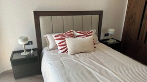 Ein ordentlich bezogenes Bett mit Streifenmuster, zwei Nachttische mit Lampen und ein hölzernes Kopfteil.