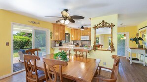 A spacious kitchen with wooden cabinets, a dining table with chairs, and a ceiling fan. - Hale Hauoli - lovely home, near golf & beaches (Princeville)