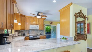 A kitchen with wooden cabinets, a microwave, a stove, and a ceiling fan. - Hale Hauoli - lovely home, near golf & beaches (Princeville)