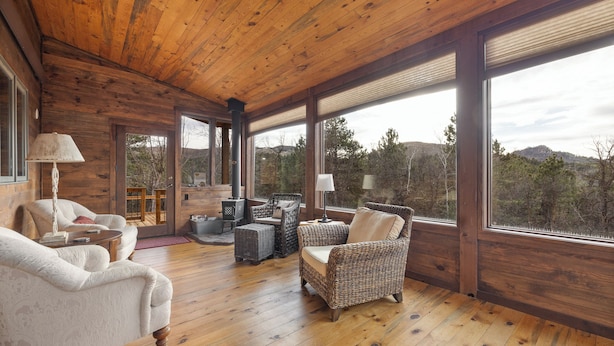 A spacious wooden-floored room with large windows, wicker furniture, and a fireplace. - 2 Miles to Deadwood! 3.5 Acres w/ 4,100 Sq. Ft - Hot Tub, Paved! (Sturgis)