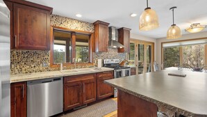 A modern kitchen with wooden cabinets, a stone backsplash, and pendant lighting. - 2 Miles to Deadwood! 3.5 Acres w/ 4,100 Sq. Ft - Hot Tub, Paved! (Sturgis)
