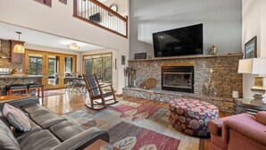 A spacious living room with a stone fireplace, a large flat-screen TV, and a high ceiling with exposed wooden beams. - 2 Miles to Deadwood! 3.5 Acres w/ 4,100 Sq. Ft - Hot Tub, Paved! (Sturgis)