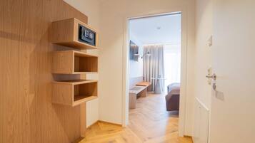 A hallway with wooden shelving, a bench, and a door leading to a room with a bed and curtains.