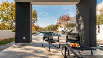 Une terrasse extérieure moderne avec une piscine, des chaises longues et une table garnie de fruits.