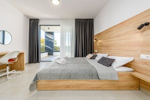 Et moderne hotelværelse med en stor seng, et træhovedgærde, et skrivebord med stol og udsigt til det fri.