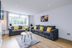 A modern living room with two grey sofas, a round coffee table, and a large window providing natural light.