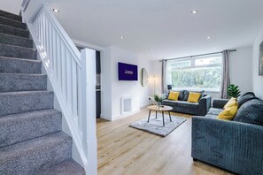 A modern living room with a staircase, a sofa set, and a large window. - M22 | Near Airport | Parking | WiFi | 15% Off (Wythenshawe)