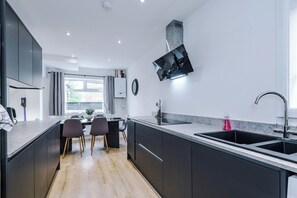 A modern kitchen with a central island, dark cabinetry, a built-in oven, and a window providing natural light.