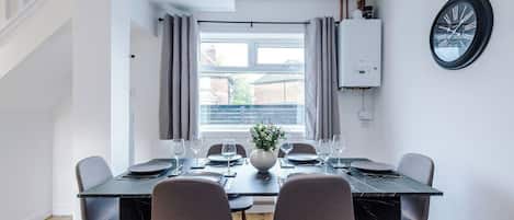 A dining area with a table set for four, a potted plant, and a window with curtains.