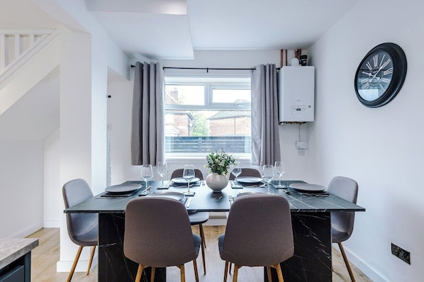 A dining area with a table set for four, a potted plant, and a window with curtains.