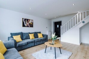 A modern living room with a grey sofa, a round coffee table, and a staircase with white railings. - M22 | Near Airport | Parking | WiFi | 15% Off (Wythenshawe)