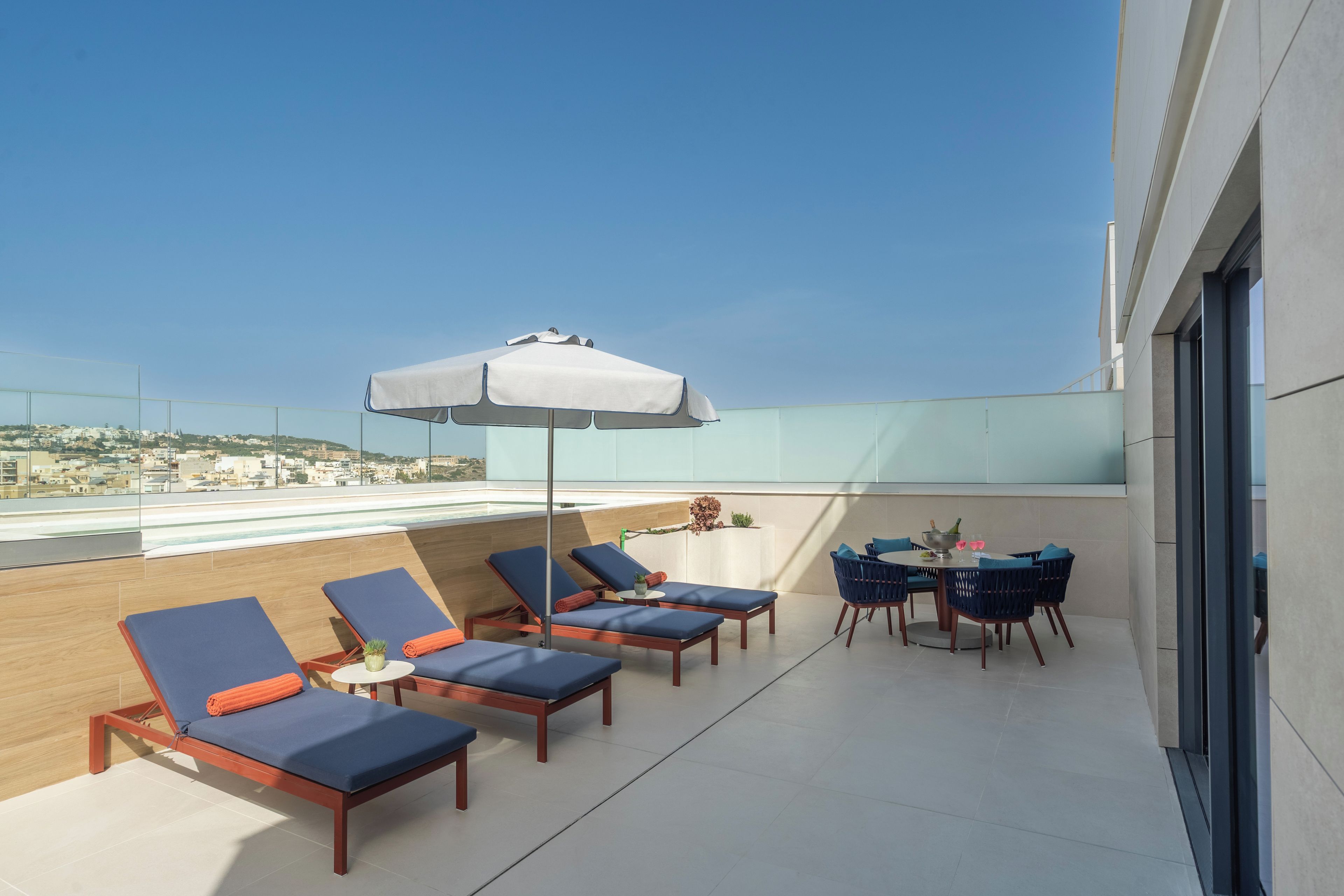 Una terraza en la azotea con sillones de descanso, una mesa con sillas y un gran parasol.