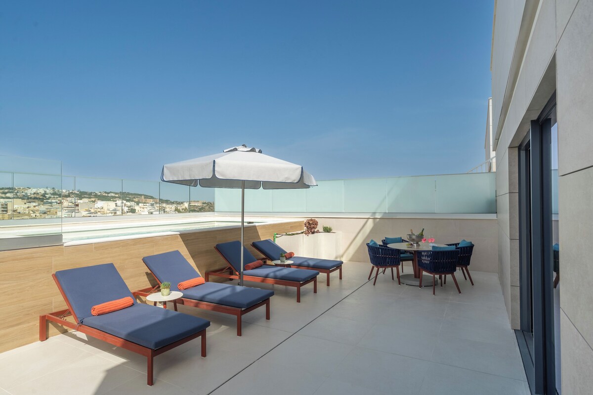 Eine Dachterrasse mit Liegestühlen, einem Tisch mit Stühlen und einem großen Sonnenschirm.