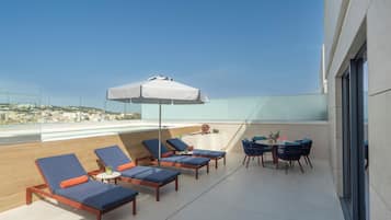 Eine Dachterrasse mit Liegestühlen, einem Tisch mit Stühlen und einem großen Sonnenschirm.