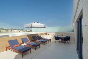 A rooftop terrace with lounge chairs, a table with chairs, and a large umbrella. - Hard Rock Hotel Malta (St. Julian's)