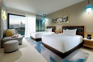 A modern hotel room with two beds, a sofa, a small ottoman, and a large window offering a city view. - Hard Rock Hotel Malta (St. Julian's)