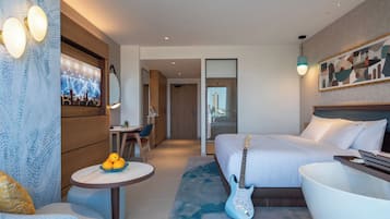 A modern hotel room with a bed, a desk, a chair, a guitar, and a television on the wall.