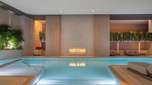 Un área de piscina interior moderna con una barrera de vidrio transparente, un cartel de spa y sillones de descanso.