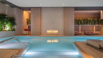 A modern indoor pool area with a clear glass barrier, a spa sign, and lounge chairs.
