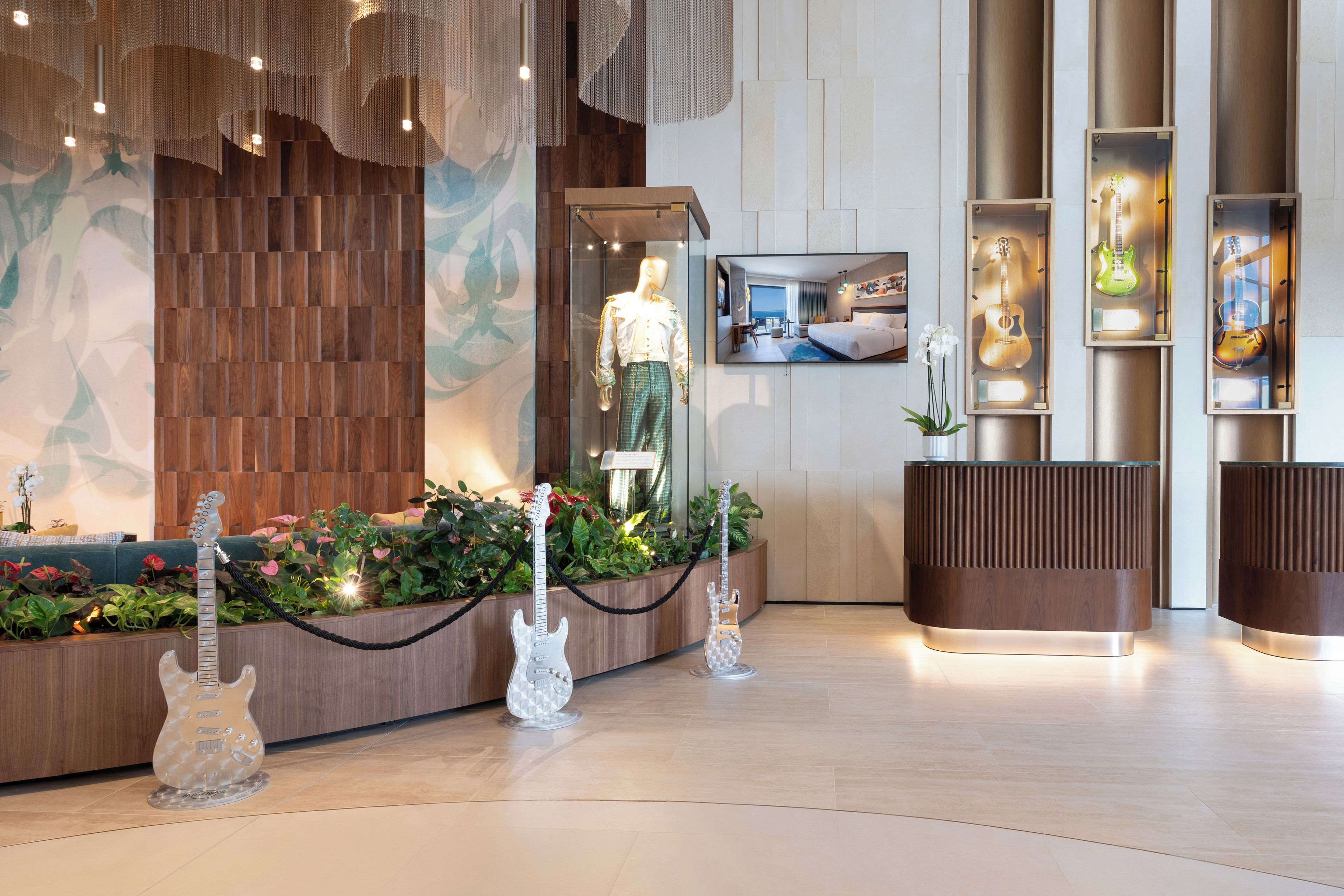 A hotel lobby with a reception desk, a mannequin dressed in a white shirt and green pants, and a large wall mural.
