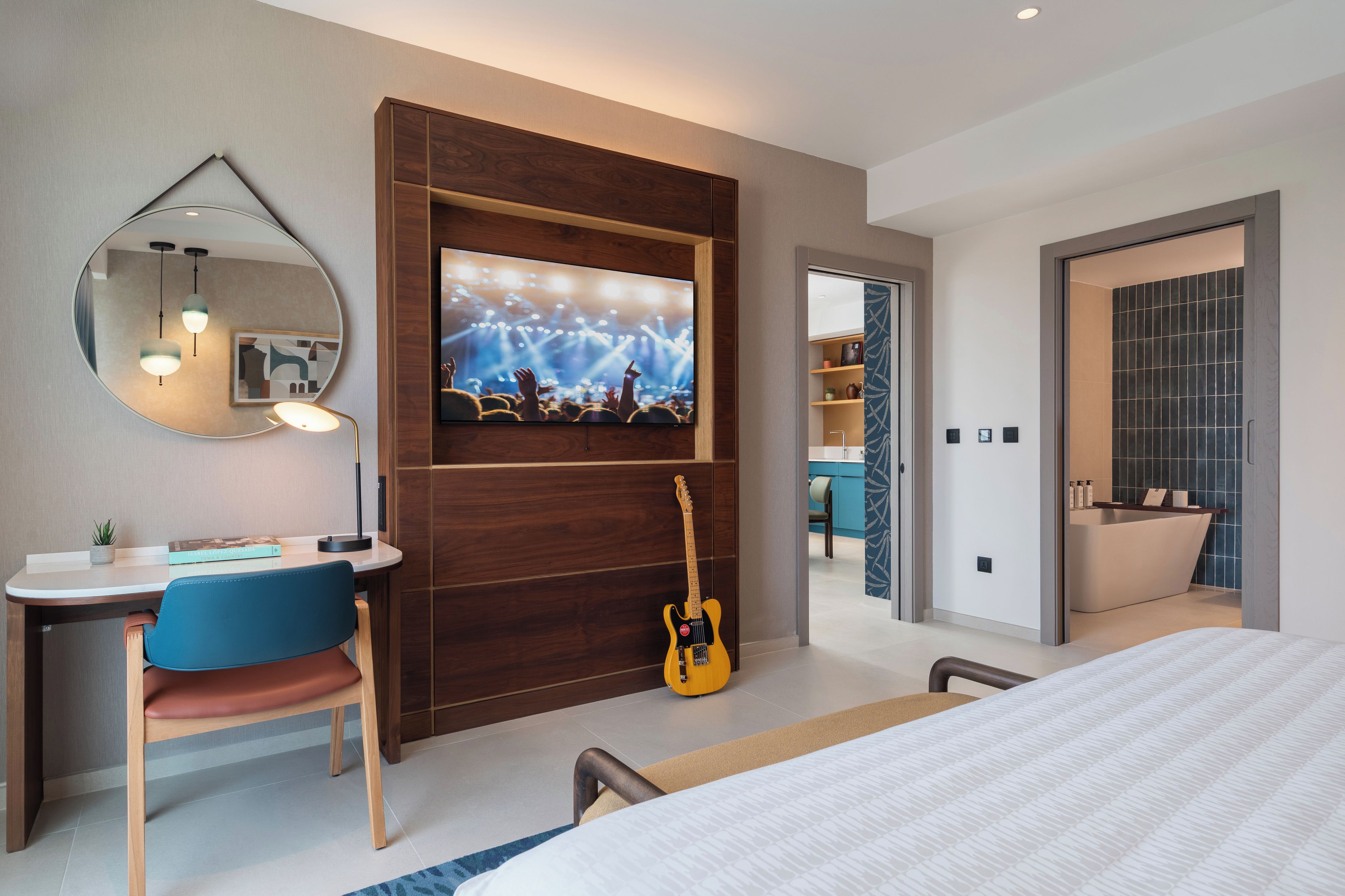 Ein modernes Hotelzimmer mit einem Bett, einem Schreibtisch mit Stuhl, einem Fernseher und einer Gitarre.