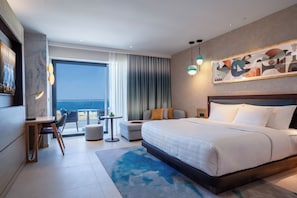 A modern hotel room with a large bed, a desk, a chair, a dining table, and a view of the sea. - Hard Rock Hotel Malta (St. Julian's)