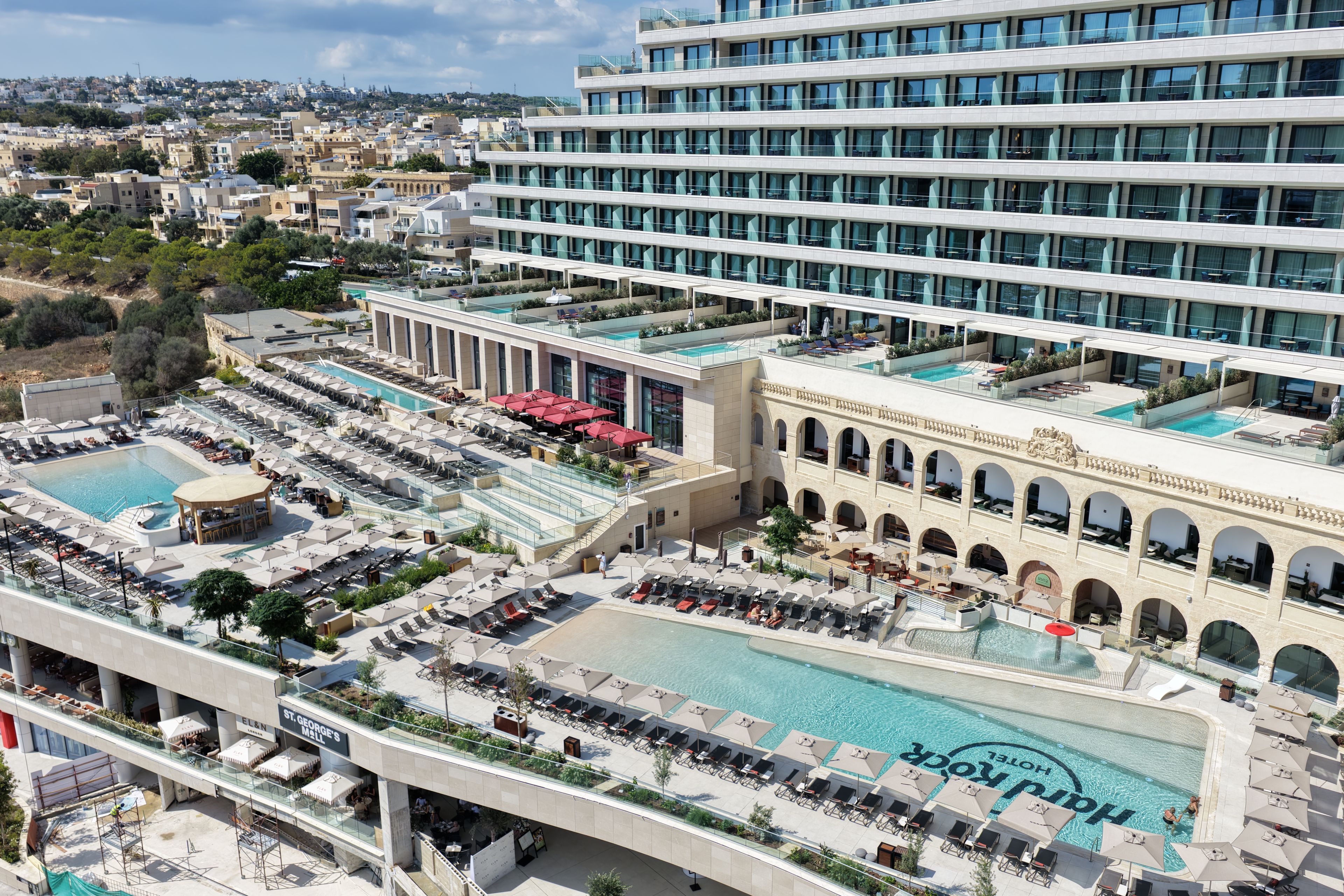 Un hotel con múltiples piscinas, zonas de estar al aire libre y una terraza en la azotea.