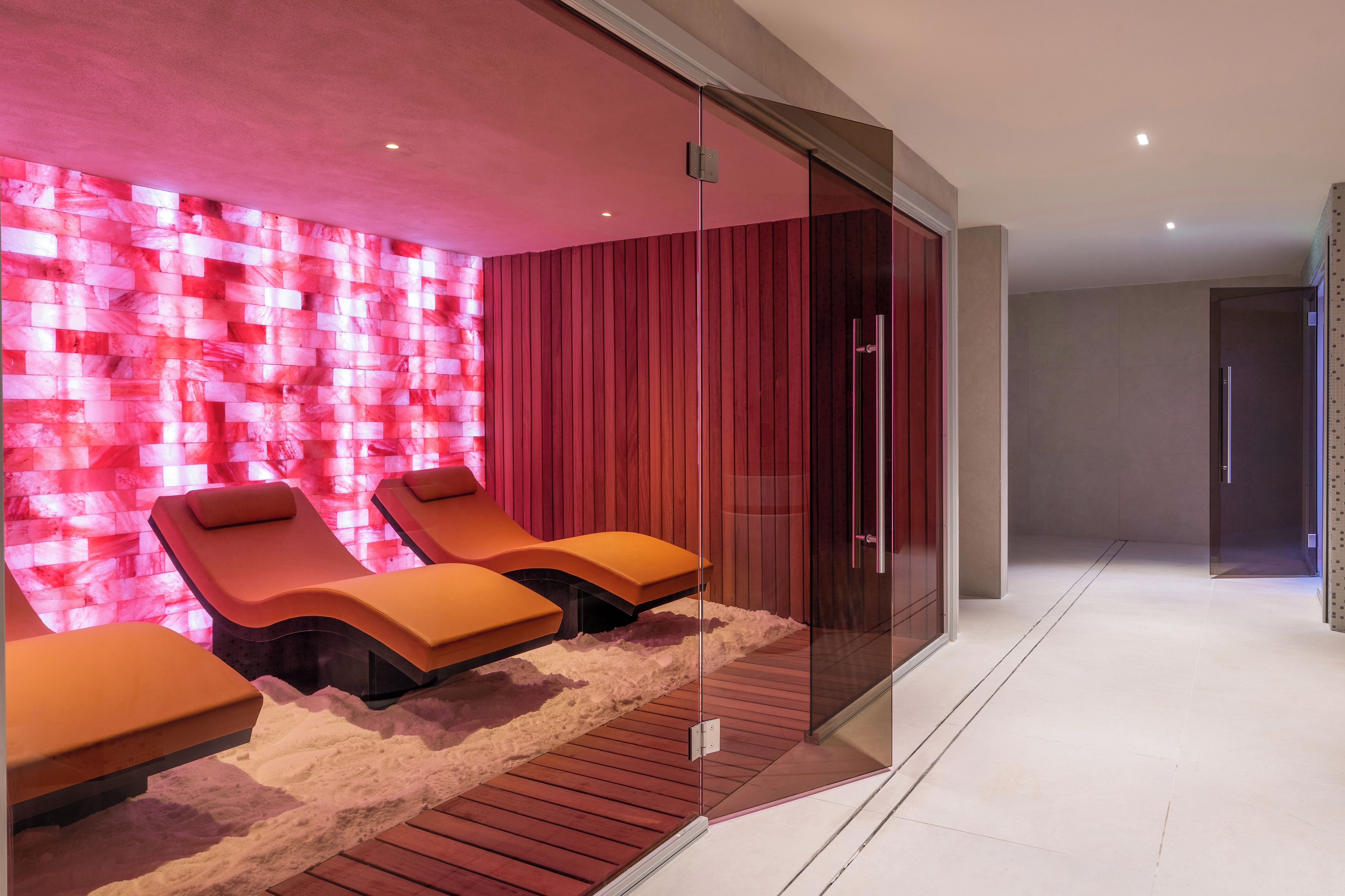 Un moderno spa con tres sillas de masaje, una pared roja con textura y un separador de vidrio.
