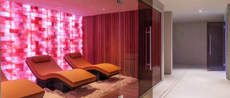 Un moderno spa con tres sillas de masaje, una pared roja con textura y un separador de vidrio.
