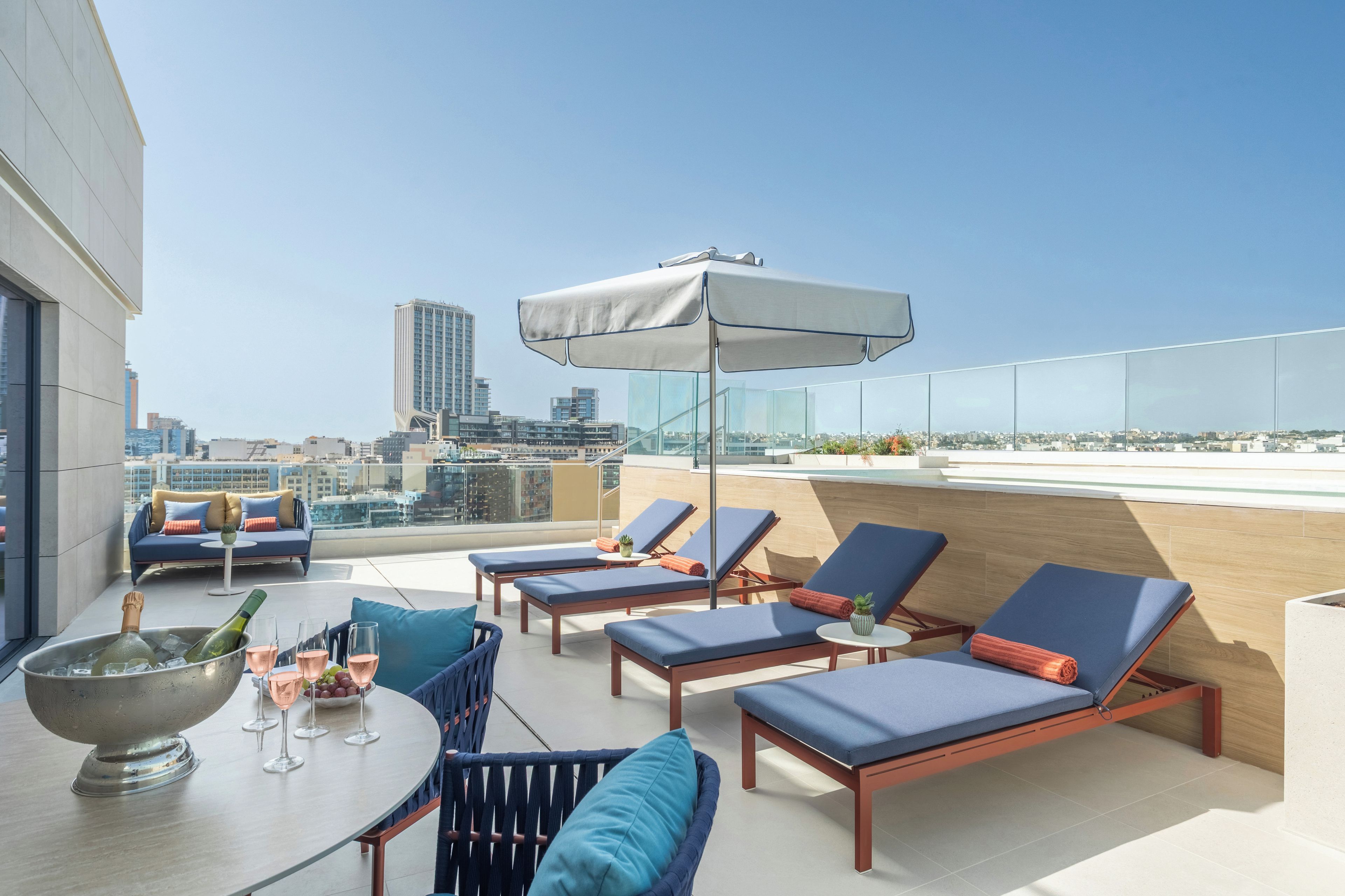 Une terrasse sur le toit, avec des chaises longues, une table avec des boissons et une vue sur la ville.
