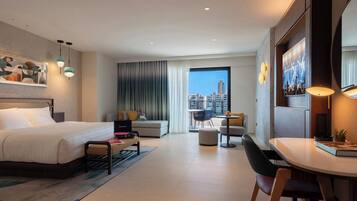 Habitación de hotel moderna con una cama grande, un escritorio, un comedor y vistas a la ciudad.