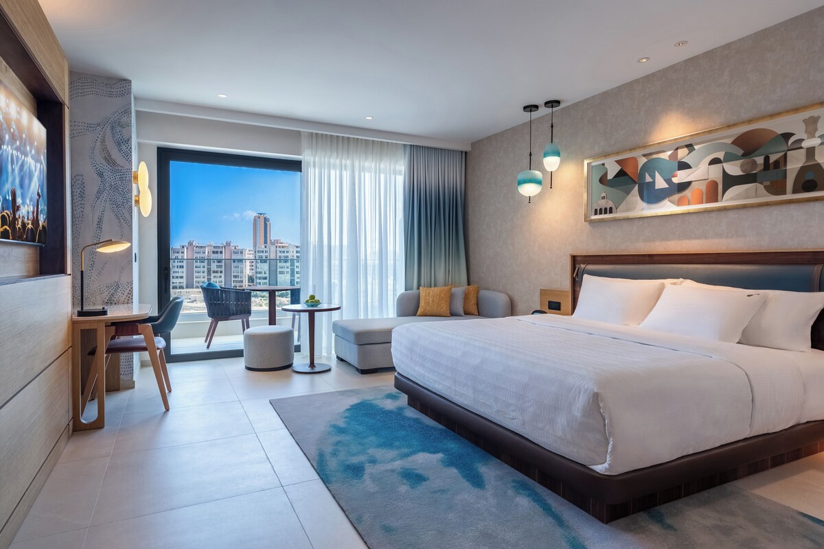 Ein modernes Hotelzimmer mit einem großen Bett, einem Schreibtisch, einem Stuhl und Blick auf die Stadt.