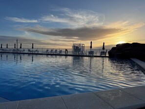 A swimming pool with a sunset view, a fence, and lounge chairs. - Ocean & City View-King Bed-Relaxing (Daytona Beach)