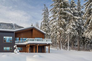 Een modern gebouw met twee verdiepingen en een balkon, omringd door met sneeuw bedekte bomen.