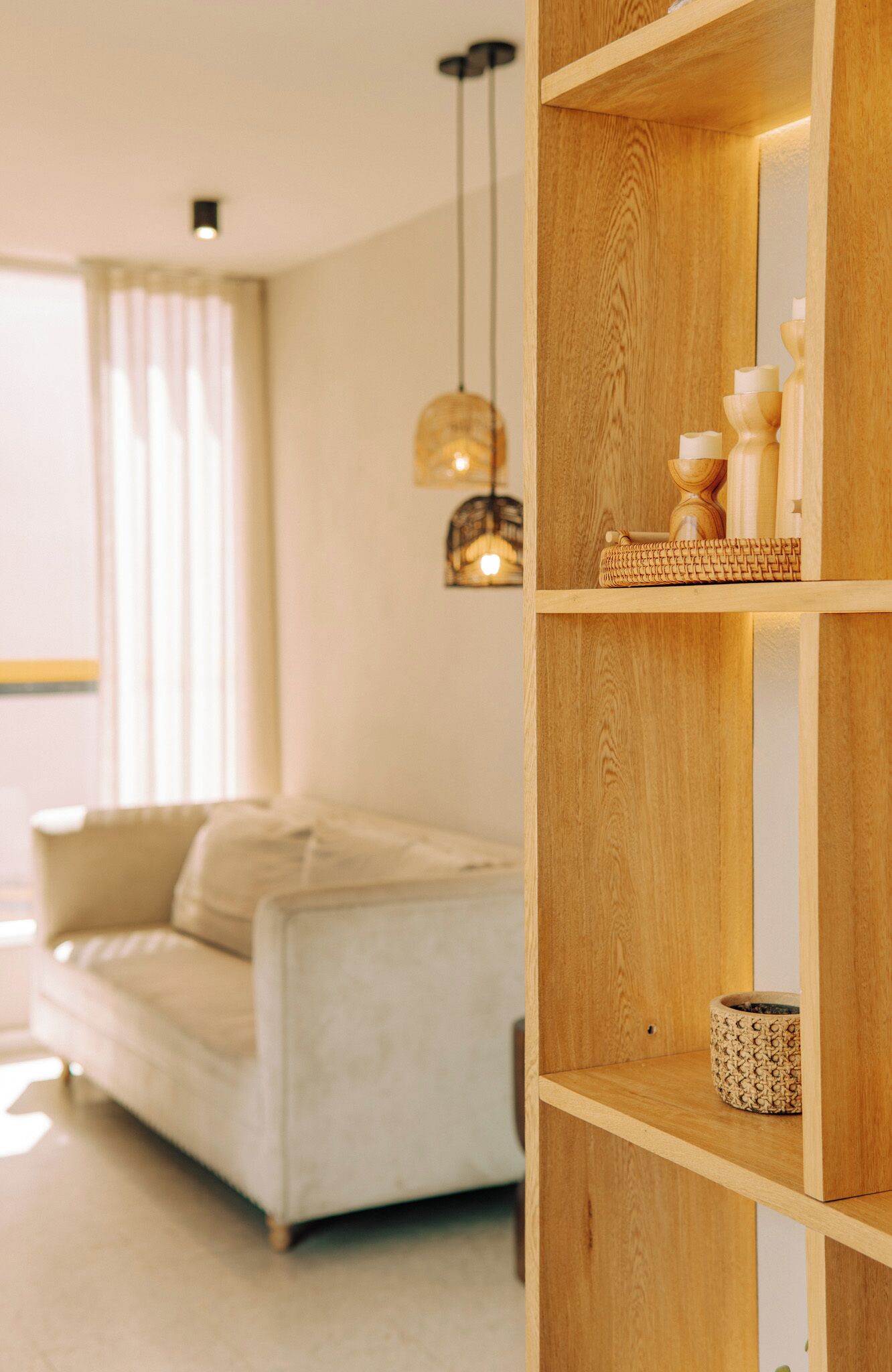 Un salon moderne avec un canapé de couleur claire, des étagères en bois ornées d’objets décoratifs et un éclairage suspendu.