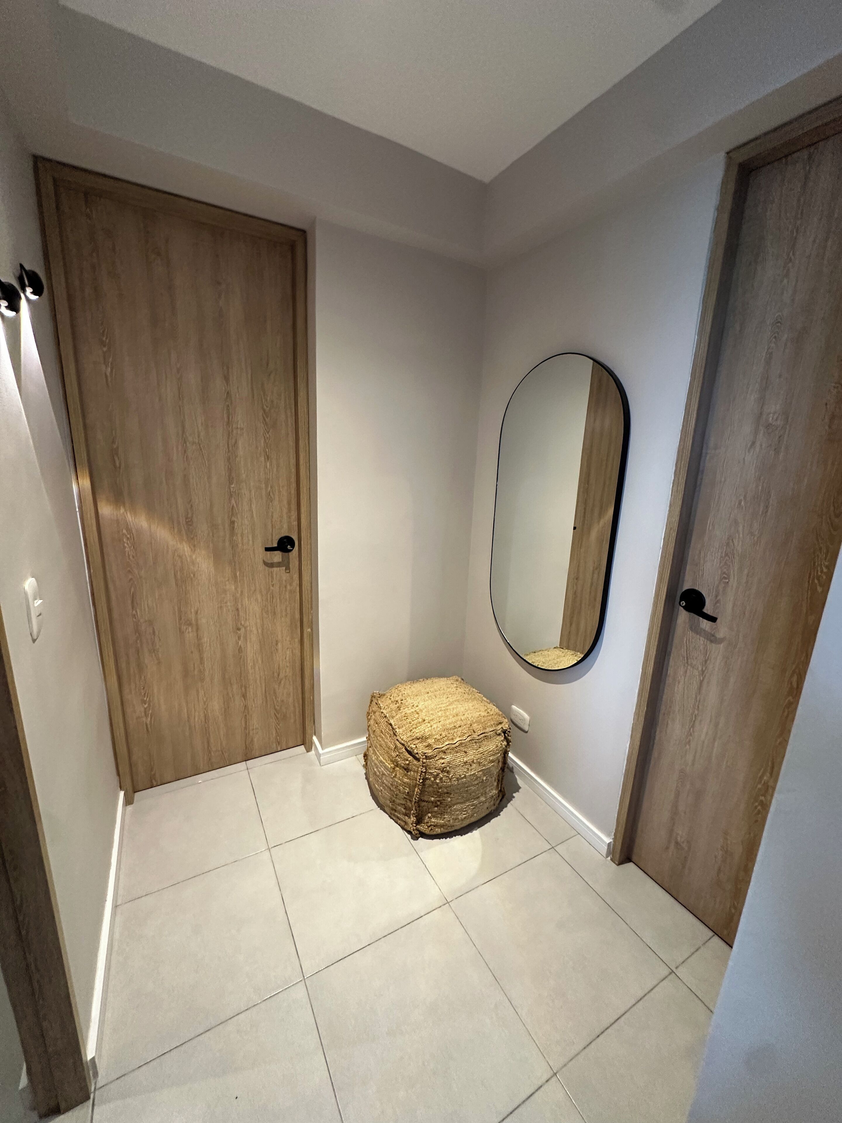 A hallway with wooden doors, a round mirror on the wall, and a woven stool on the floor.