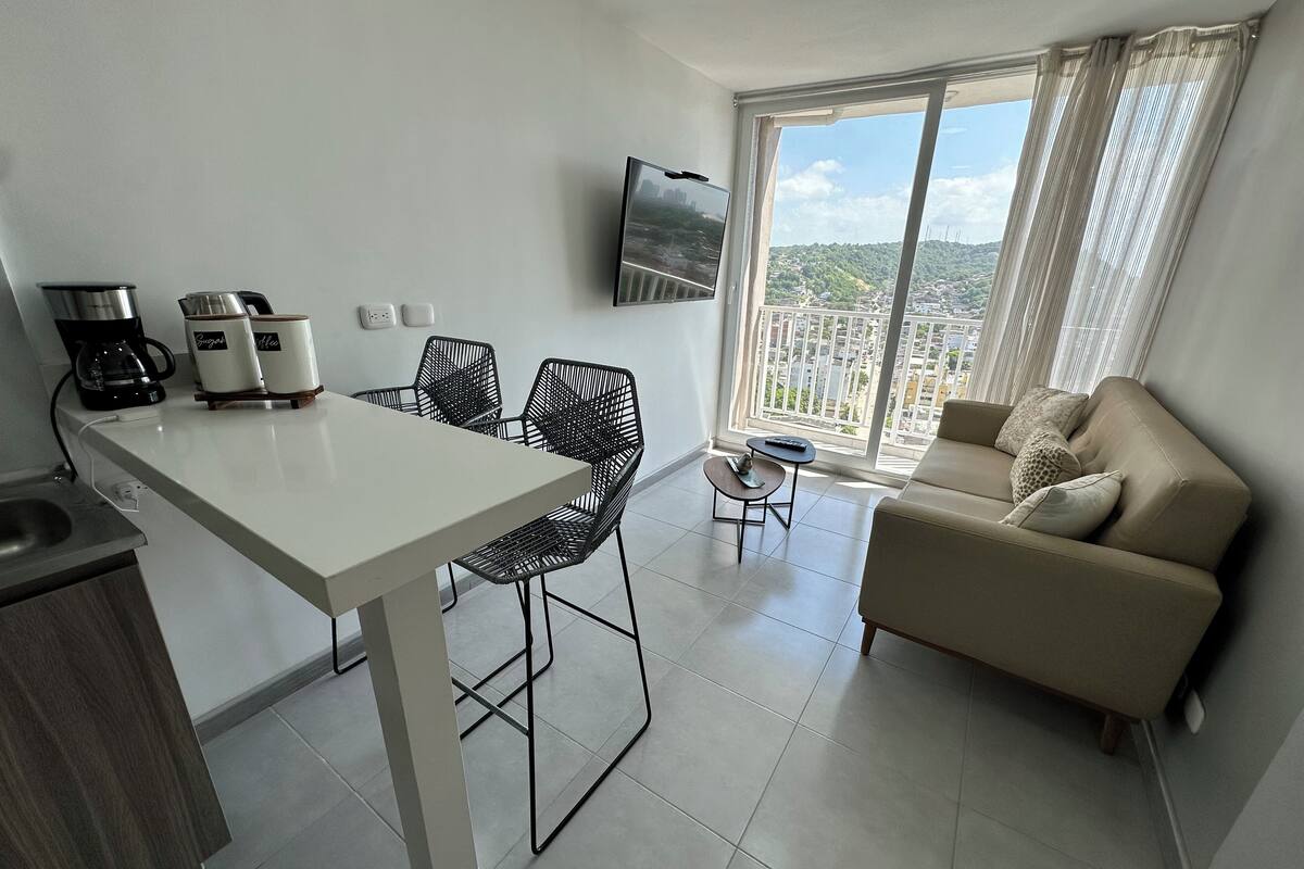Um espaço de estar moderno com área de jantar, sofá e varanda com vista para a cidade.