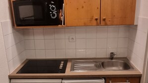 Een kleine keuken met een magnetron, fornuis, spoelbak en een kleine koelkast.