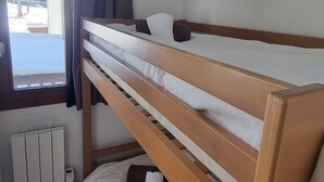 Een slaapkamer met een stapelbed, een raam, een radiator en een houten hoofdbord.