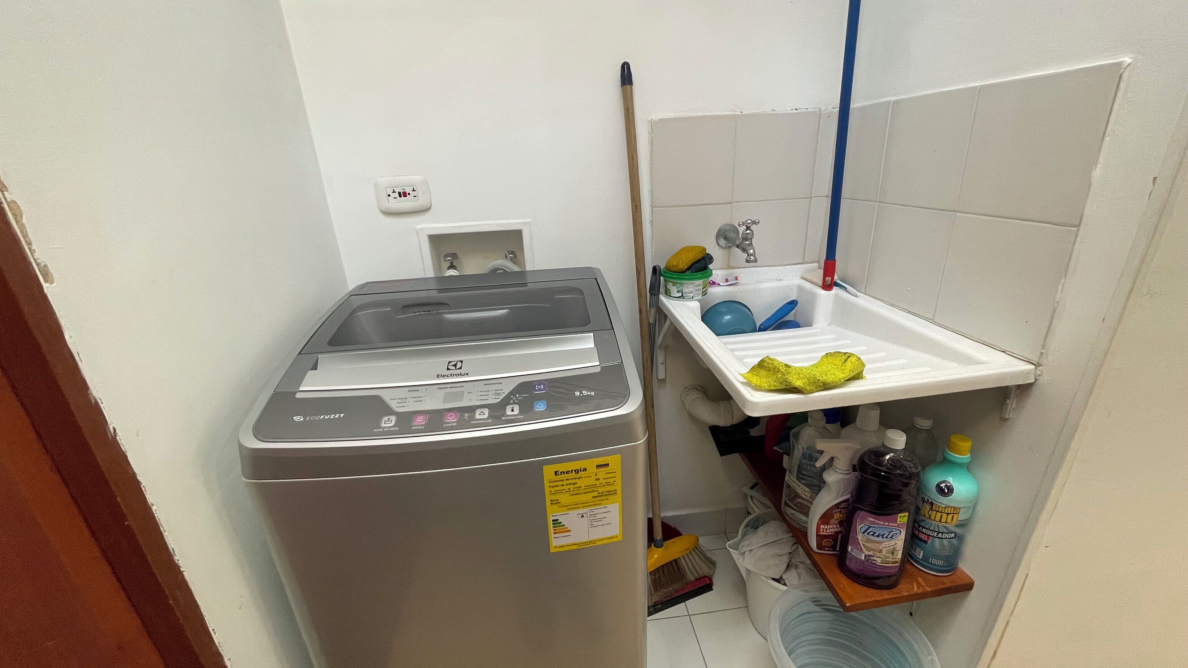 A compact laundry area with a washing machine, a sink with a drying rack, and cleaning supplies.