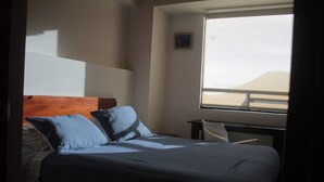 Ett sovrum med en säng, kuddar, ett skrivbord och ett fönster med utsikt.