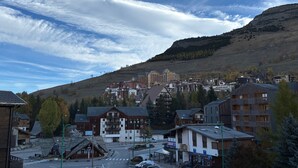 A town with a mix of traditional and modern buildings, a main road, and a hilly backdrop. - Beautiful apartment, sleeps 5, mountain view (Les Deux Alpes)