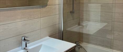 A modern bathroom with a white sink, a glass shower enclosure, and wooden paneling on the walls.