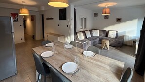 A modern kitchen with a dining area, a gray sofa, and a wooden dining table set for four. - Beautiful apartment, sleeps 5, mountain view (Les Deux Alpes)