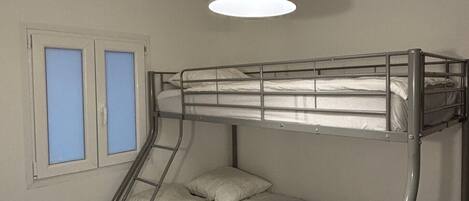 Dormitorio con literas, una cama individual y un ventanal con cristales azules.