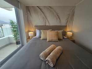 Ein Hotelzimmer mit einem großen Bett, zwei Nachttischlampen und Blick auf die Stadt durch ein großes Fenster.